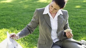 businesswoman sitting in a lawn eating a sandwich and reading a newspaper